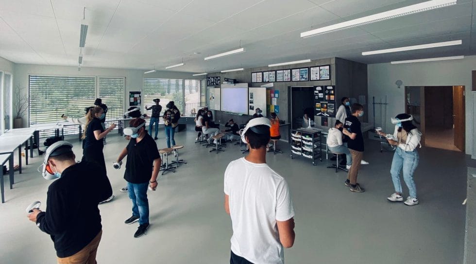 Group of students wearing VR headsets and holding controllers in a spacious classroom, participating in an interactive learning activity.