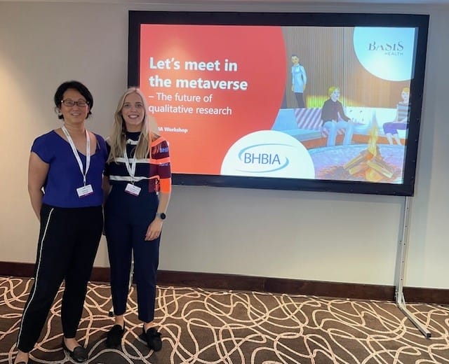 Two Basis Health staff members standing in front of a presentation screen titled “Let’s meet in the metaverse – The future of qualitative research” at the BHBIA workshop.